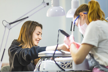 The manicurist cleans and removes the cuticle from the nail plate. Manicure process. Cut manicure technique. Special equipment for trimmed manicure.