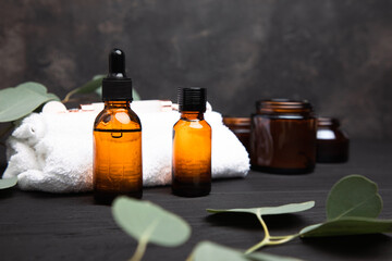 Amber bottles with facial cosmetics with a branch of eucalyptus on the dark wooden and concrete background. Front view