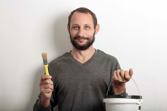 Bearded man standing with brushes and paint. Caucasian handsome male painter worker holding paint new brush. Happy painter in working clothes hold painting tools for building and construction work
