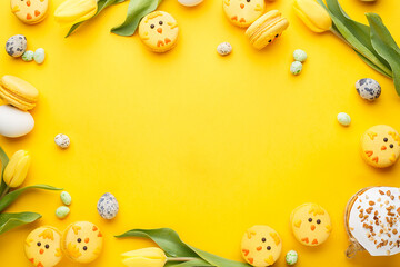 Frame composition made of macaroon chicks, tulips, candy chocolate eggs, quail eggs and easter bread over yellow background. Top view, copy space. Easter background or greeting card. Holiday symbol