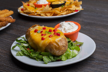 Baked potatoes with cheese topping and dip on a wooden table 