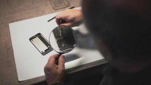 an adult man in the workshop repairs a smartphone. the master uses a magnifying loupe.close-up. High-quality shooting in 4k format