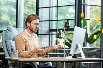 Financial problems. A young male businessman is sitting at a desk in the office and looking...
