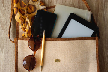 Retro bag with book, tablet, phone, pen, glasses and leopard pattern scarf. Top view, wooden background.