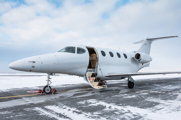 Modern white business jet with an opened gangway door at the winter airport apron
