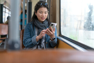 Young and happy asian female woman using smartphone while sitting near the window in the public...