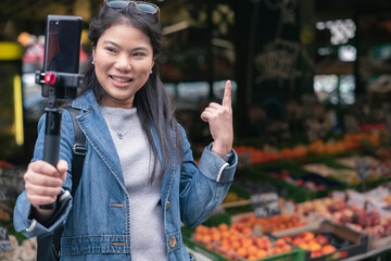 asian female blogger vlogger record vlog streaming video hold phone on selfie stick in open market urban city.Young Asian female tourist woman holding smartphone and recording videos travel concept - Powered by Adobe