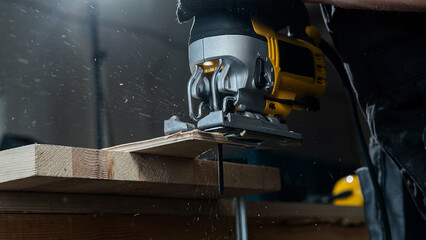 Close-up of a man cutting a wooden plank with an electric jigsaw in a workshop.