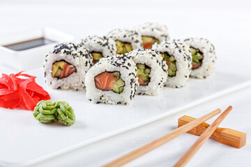 Sushi with salmon on a white plate with wasabi, ginger, soy, chopsticks on a white background