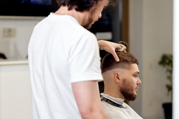 Barber trim hair with clipper on handsome bearded man