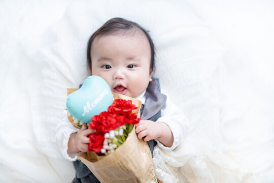 母の日にカーネーションの花束をママにプレゼントで渡そうとしながらにこにこ笑顔になる赤ちゃん