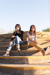 Fototapeta na wymiar Airy full length shot of diverse teenagers outdoors while sitting on stairs in sunlight