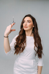 young dark-haired curly woman doctor in a white coat holds an insudin syringe for injection in her hands. Cosmetologist in a beauty salon preparing for a beauty procedure