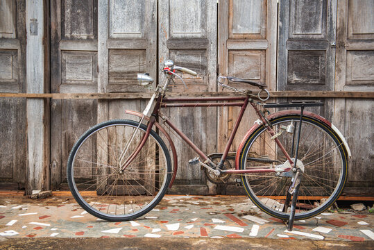 Vintage bicycle on old rustic dirty wall house, many stain on wood wall. Classic bike old bicycle on decay brick wall retro style. Cement loft partition and window background.