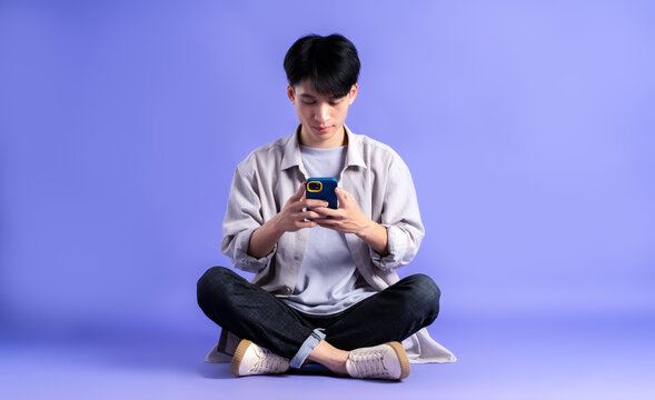 full body image of young asian man using phone on purple background