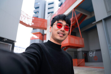 young asian man wearing cool red glasses taking point of view selfie smiling life style