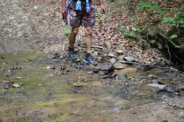 Tourist cross a stream river during a hike in the forest