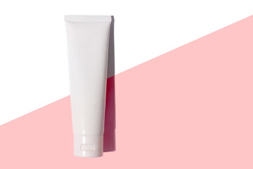 White cosmetic tube of cream with hard shadow on white and pink background.