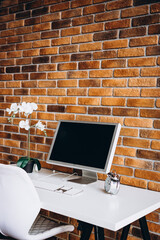 a computer, a notebook, a white orchid on a white table and a brick wall. stylish itnreyer. home office