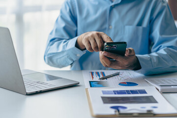 Male businessman hand using smartphone to analyze and calculate annual income and expenditure. Financial and technology charts and graphs showing market dynamics and holding smartphone at office