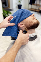 Naklejka premium Barber shaving bearded man in barber shop.