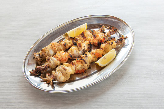 grilled fish with cuttlefish and shrimp , seasoned with lemon and spice , close-up photograph on white wooden background , horizontal