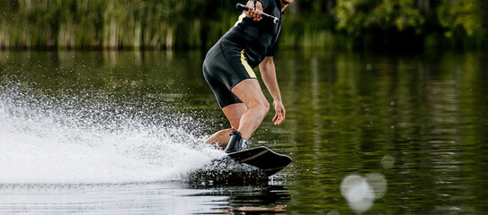 man wakeboarding on summer lake. water splashes from under board