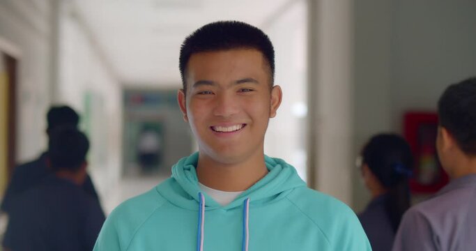 Slow motion scene of a happy smiling male high school student standing on a corridor in a school building.