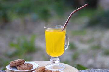 Glass of orange juice with reusable straw and two plates with cookies, served in a garden. Selective focus.