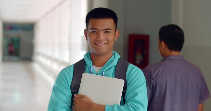 Slow motion scene of a happy smiling male high school student standing on a corridor in a school building with a laptop backpack.