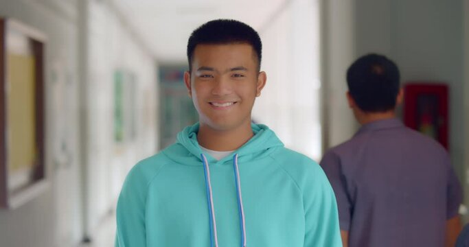 Slow motion scene of a happy smiling male high school student standing on a corridor in a school building.