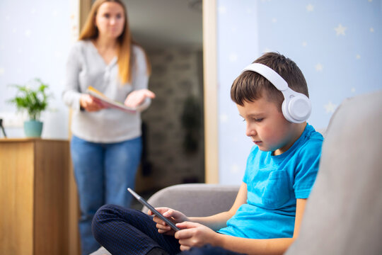 Mother scolds her son. Boy uses tablet with headphones and ignores his mom