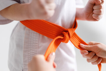 Tying an orange karate belt, close-up. © Andrii Zastrozhnov