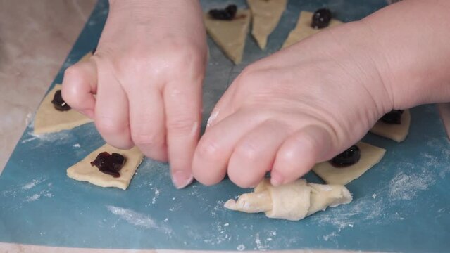 Women's hands wrap the filling in the dough when making homemade cookies.