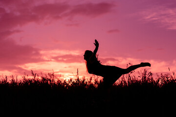 The silhouette of a trip girl over the grass on the background of a pink sunset
