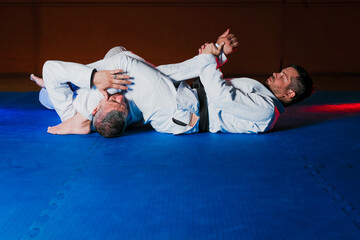 Two latin men performing martial arts and one of them practices an arm lock on the other. one of them is a black belt.