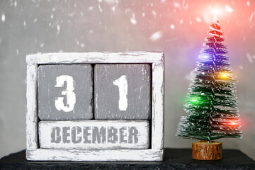 December 31 on wooden calendar background of Christmas tree with garlands and falling snow.Concept upcoming new year.