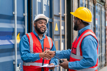 Portrait of Two African Engineer or foreman wears PPE shaking hand with cargo container background at sunset. Logistics global import or export shipping industrial concept.