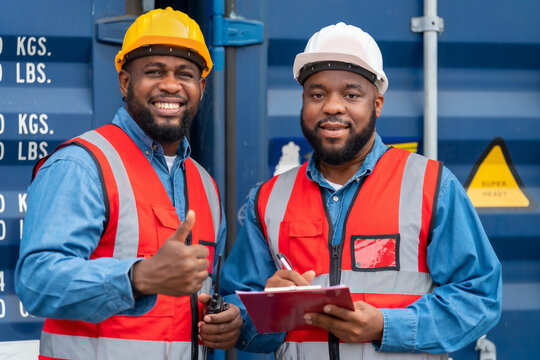 Portrait of Two African Engineer or foreman wears PPE checking container storage with cargo container background at sunset. Logistics global import or export shipping industrial concept.