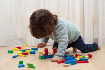 Toddler building a house with colorful wooden blocks at home.