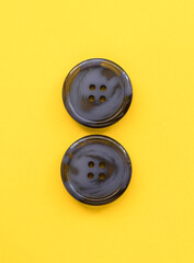Two blue plastic buttons close up on a yellow background. Sewing tools. Top view. Copy space.