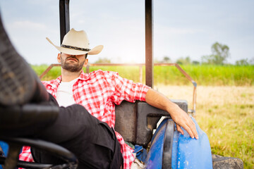 Handsome Middle East Asian man sitting on tractor and relaxing. Male farmer wearing a hat and...