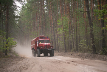 Fototapeta na wymiar Fire truck on dusty road in pine forest