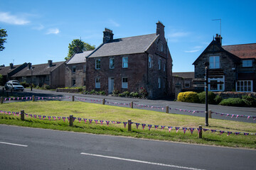Fototapeta na wymiar Bamburgh village green and cottages. Decorated with bunting during Platinum Jubilee celebrations, June 2022. Northumberland, UK