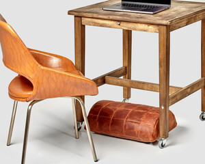 Office workspace with laptop, wooden table, chair and leather footrest
