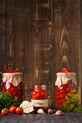 Canned cherry tomatoes fall into a jar on a wooden background with space for text