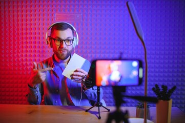 Young male technology blogger recording video blog or vlog about new smartphone and other gadgets at home studio. Blogging, Work from Home concept. Focus on gadgets at the table. Web Banner