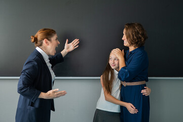 The teacher screams at the schoolgirl and her mother standing at the blackboard. 