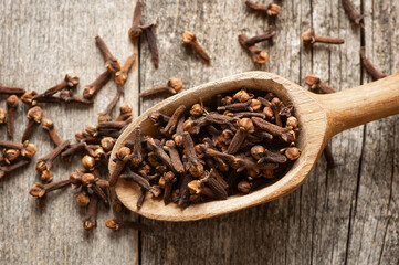 Dry cloves in wooden shovel or spoon on rustic table, fresh herb spice concept 