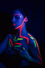 Fashion model woman in neon light, portrait of a beautiful model with fluorescent makeup, body art design in UV, painted face, colorful makeup, on a black background of a girl. 